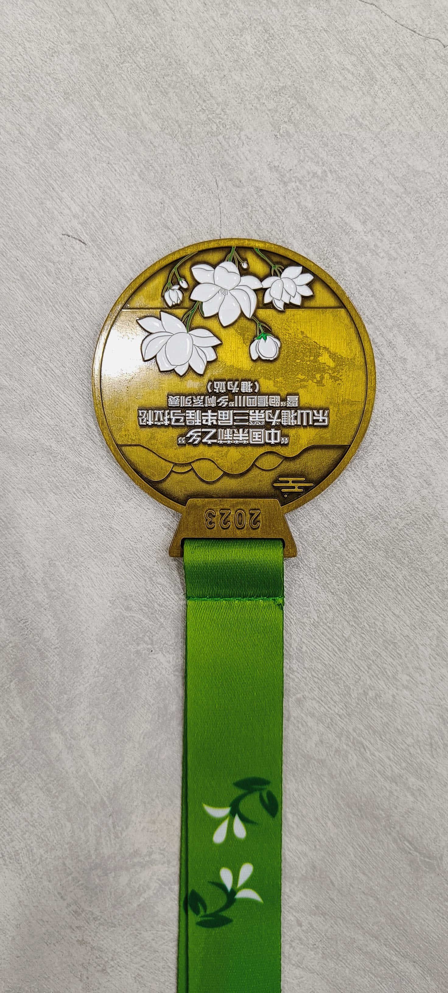 Gold award medal featuring white floral design and a green ribbon.